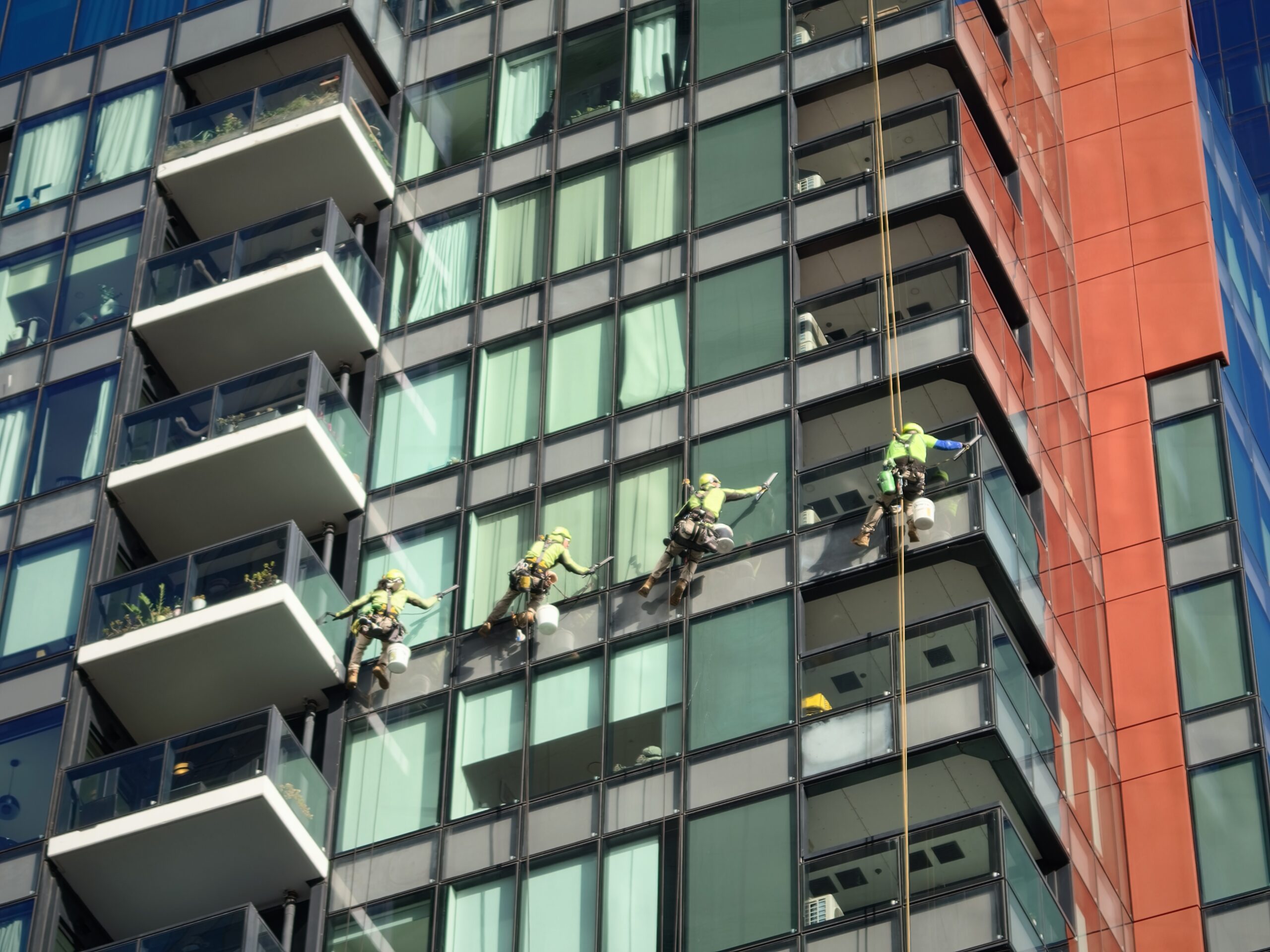 Four abseiling technicians cleaning the glass facade of a high-rise apartment building